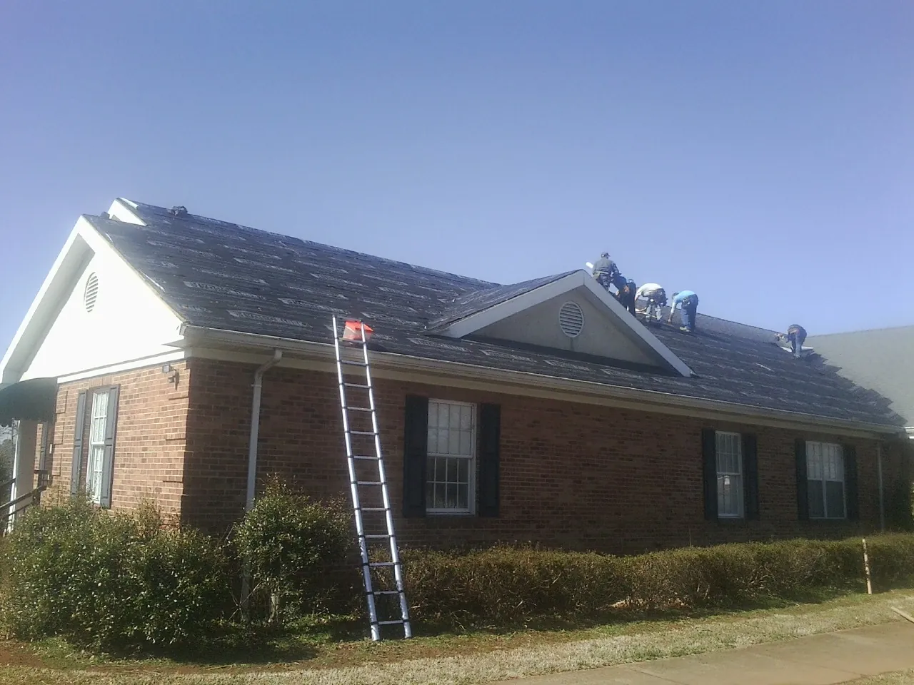 Crew tearing shingles off a brick ranch roof with a ladder set — Emergency Roof Repair work by our crew in Gladstone
