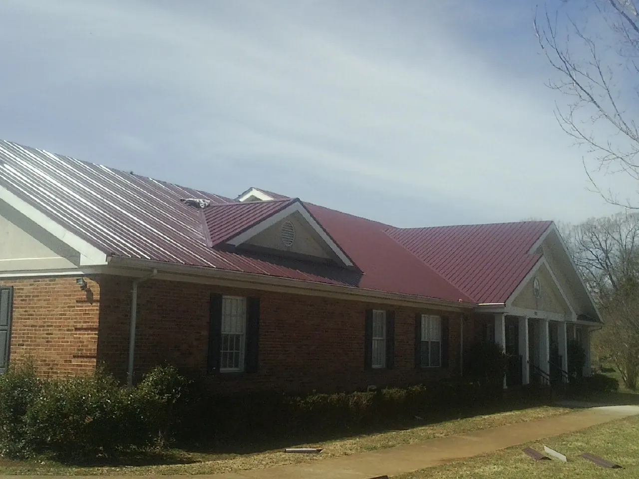 Red metal roof with gabled entries on a long brick building, from a Hail Damage Roof Repair job in Gladstone