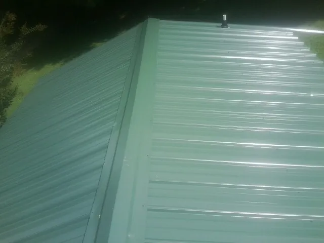 New green metal panels meeting at the ridge of a roof — Flat Roof Repair work by our crew in Gladstone