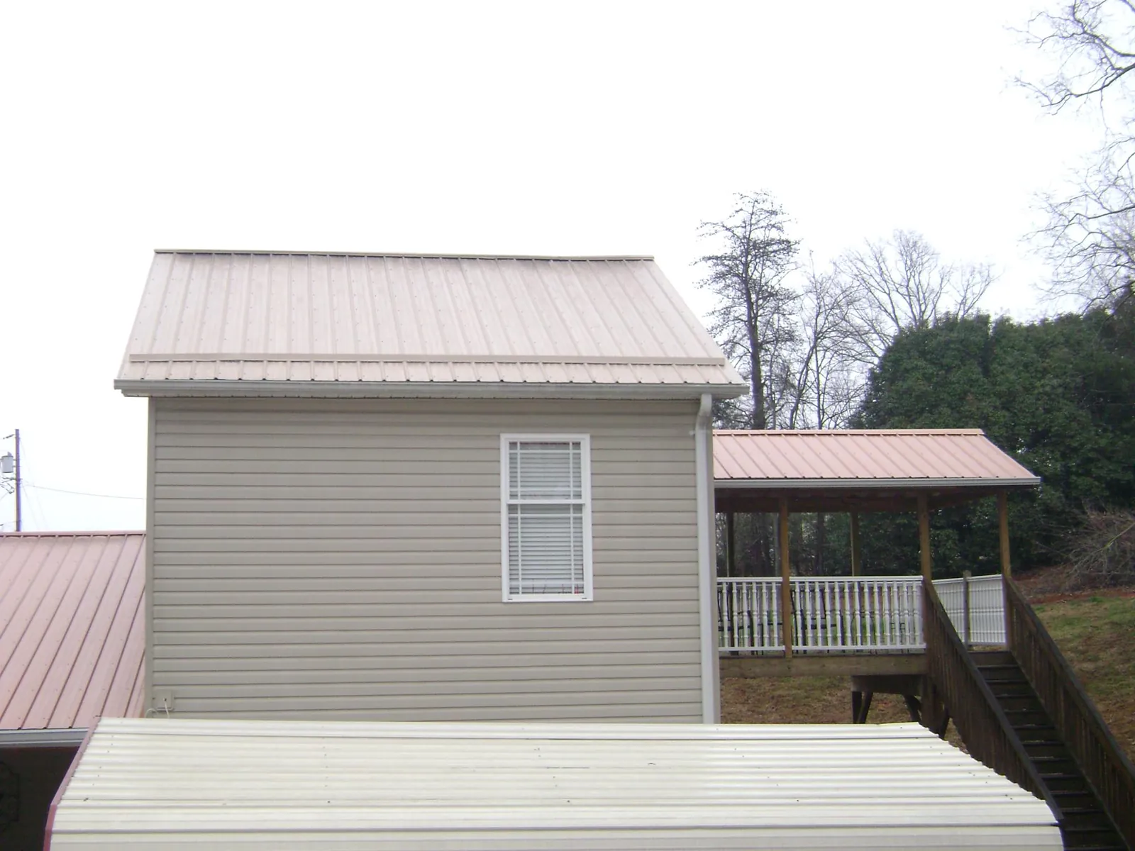 Tan metal roofs on a two story addition and attached porch, from a Roof Replacement job in Gladstone